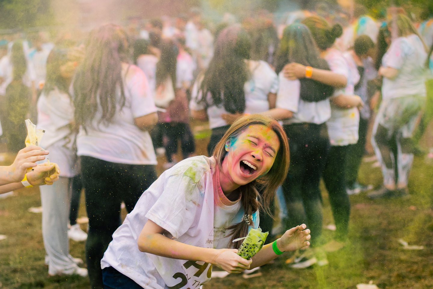 A woman laughing with closed eyes covered in colorful powder.