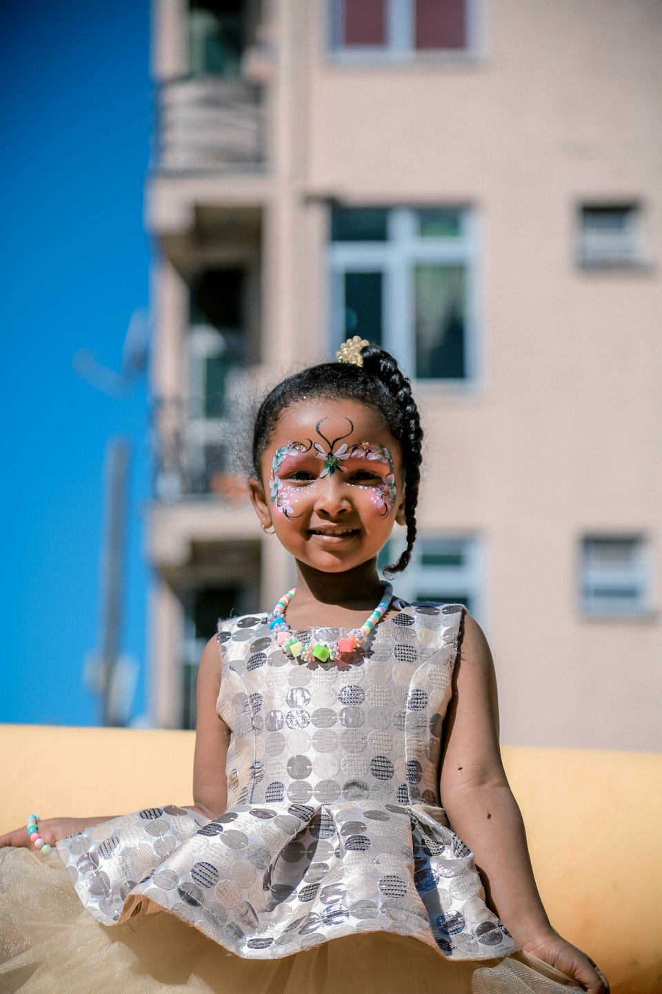 Child with butterfly face paint smiles in a patterned dress.