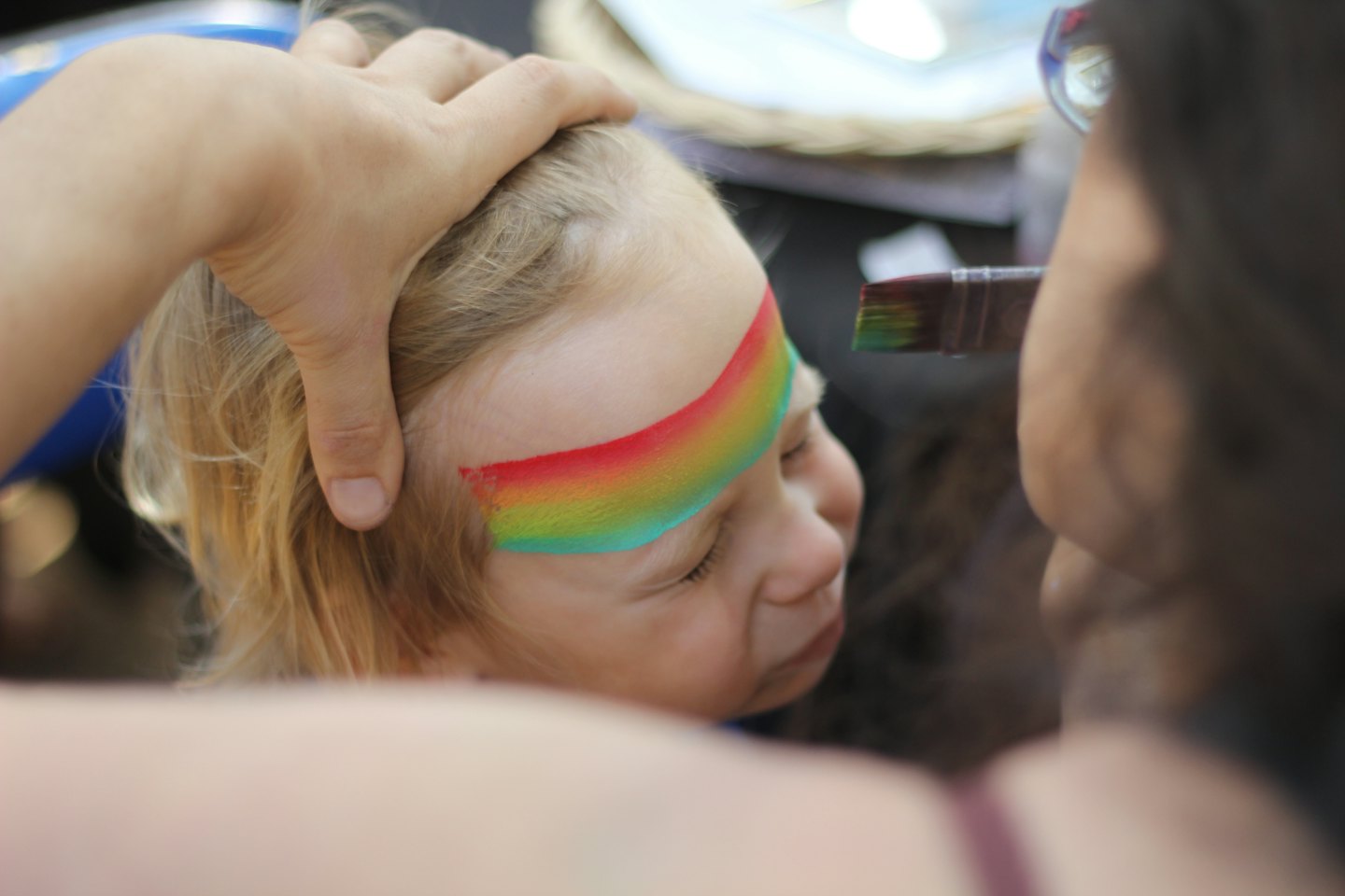 Child's forehead being painted with a rainbow design.