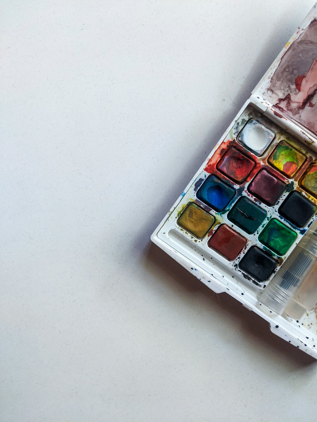 Open watercolor palette with paintbrushes on a white surface.