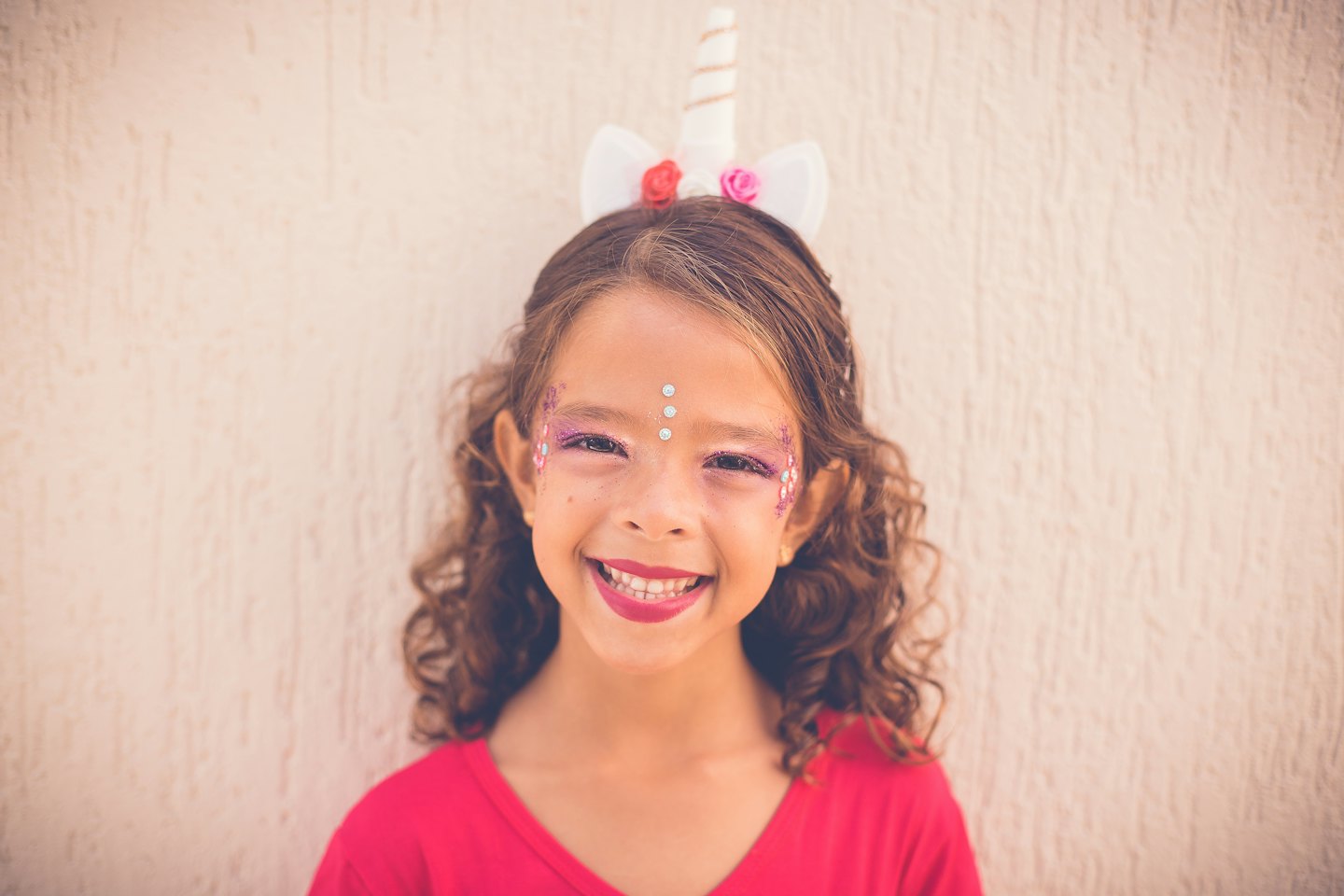 Girl with unicorn horn headband and glittery makeup smiling.