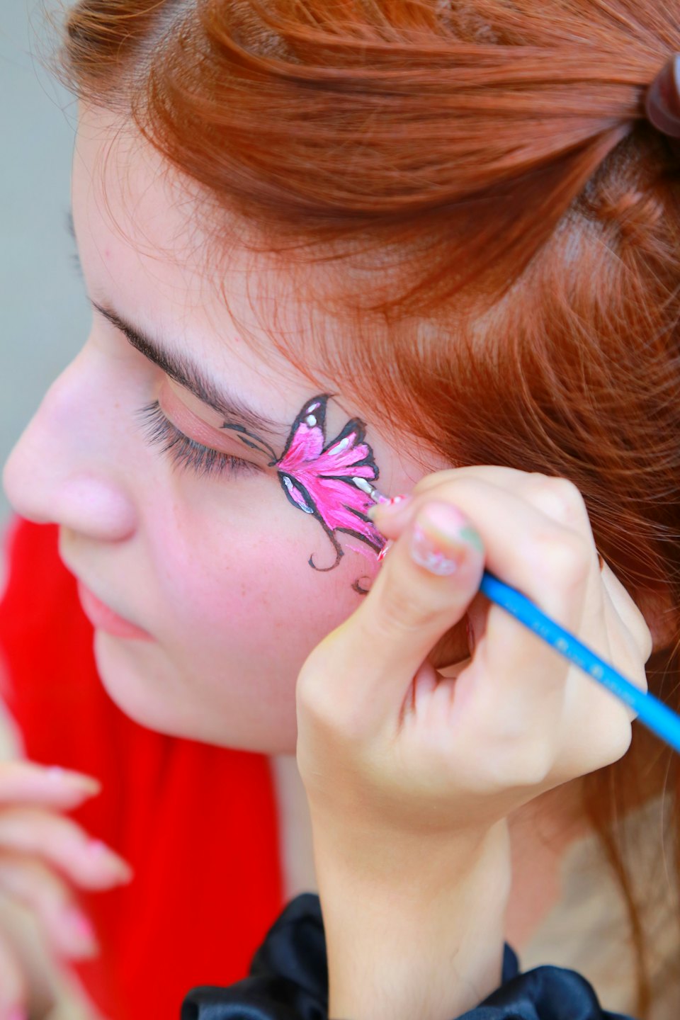 An artist paints a butterfly on a person's cheek.